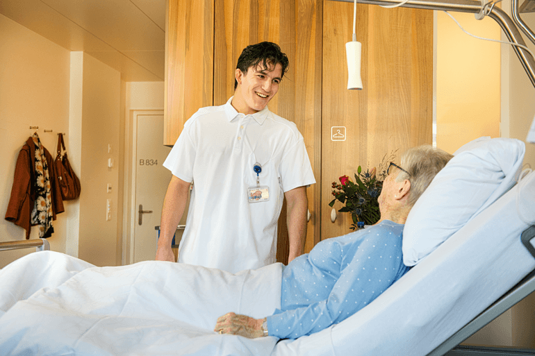 Pflegefachmann im Gespräch mit einer Patientin im Spitalzimmer