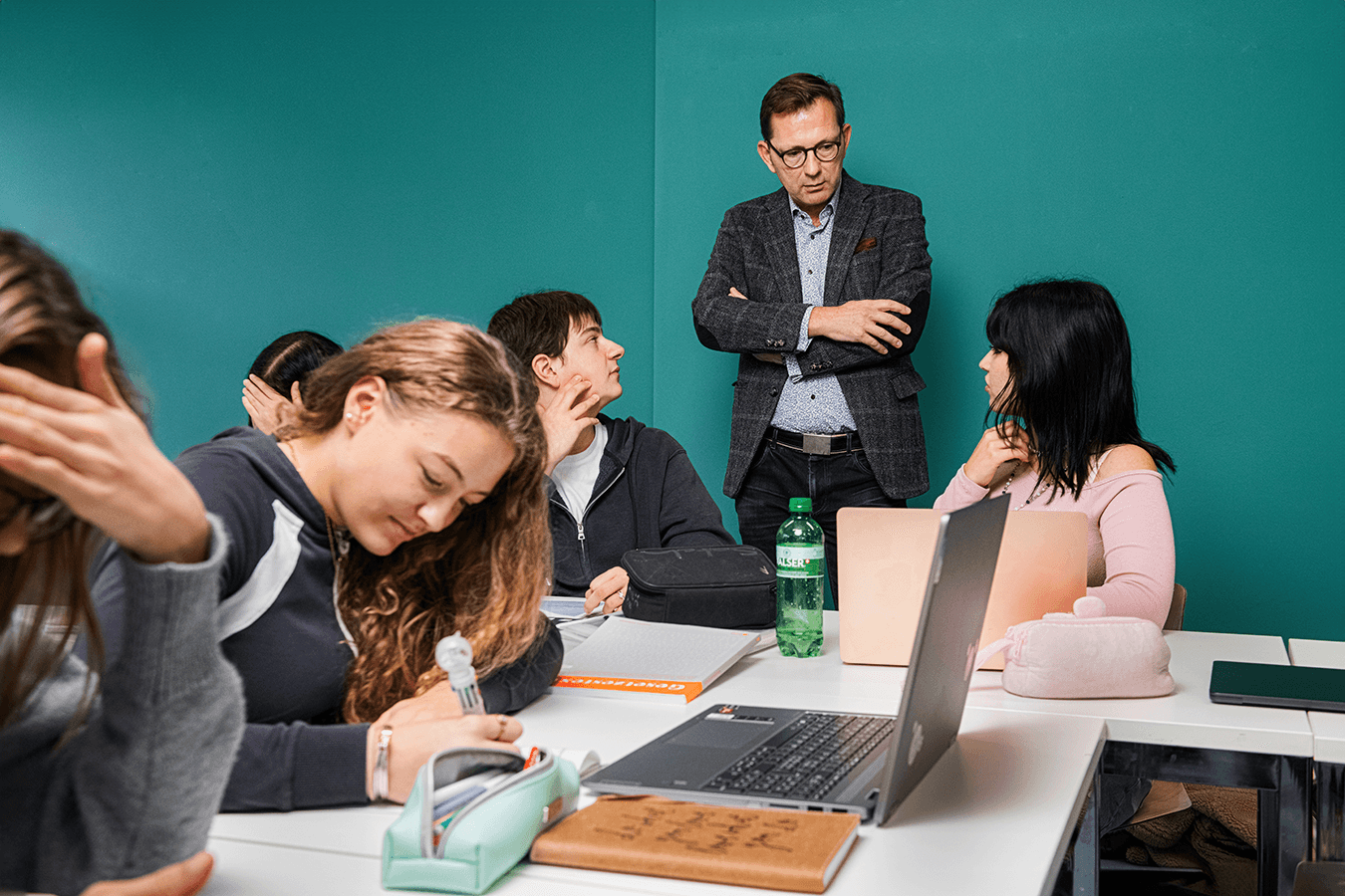 Studierende arbeiten im Unterricht an Laptops, eine Lehrperson steht daneben